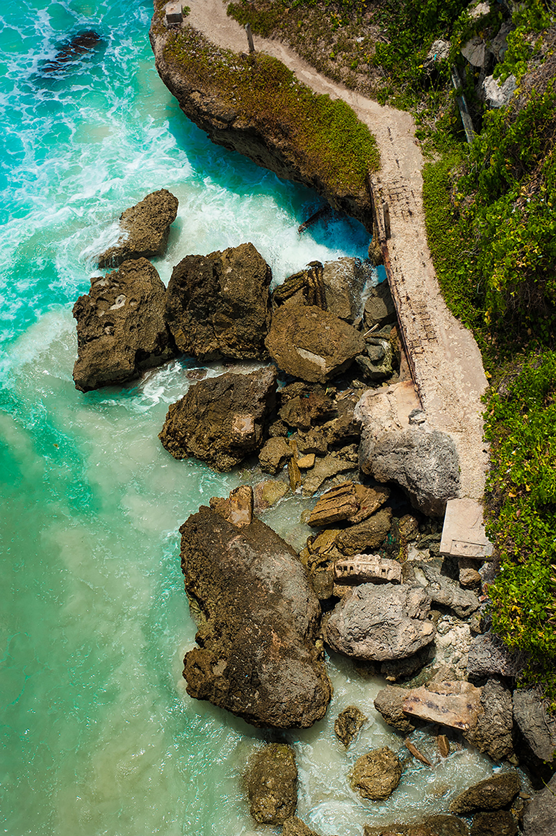 portrait photo of boulders along a teal sea and green coast line