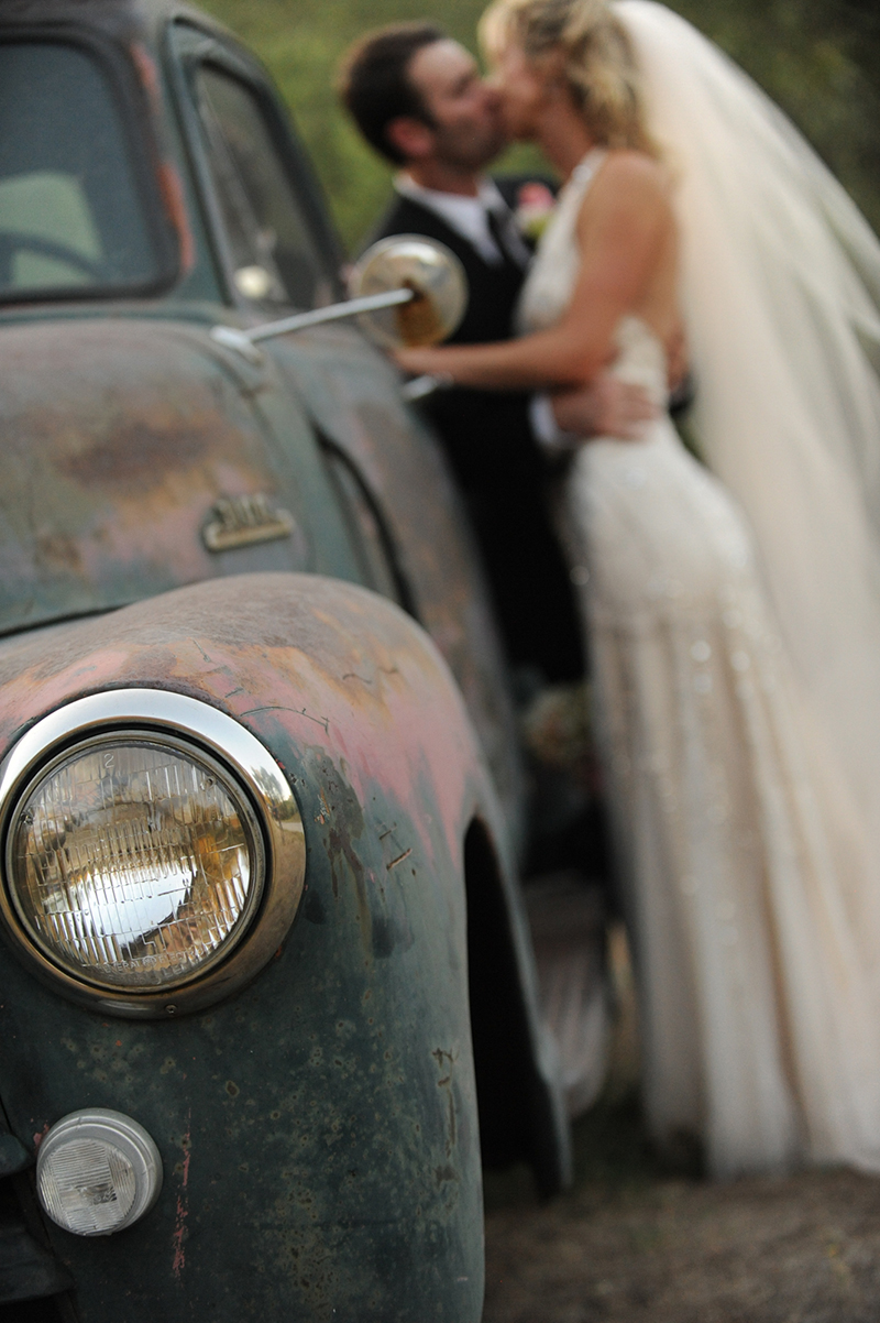 bride and groom kissing against an old rusty car