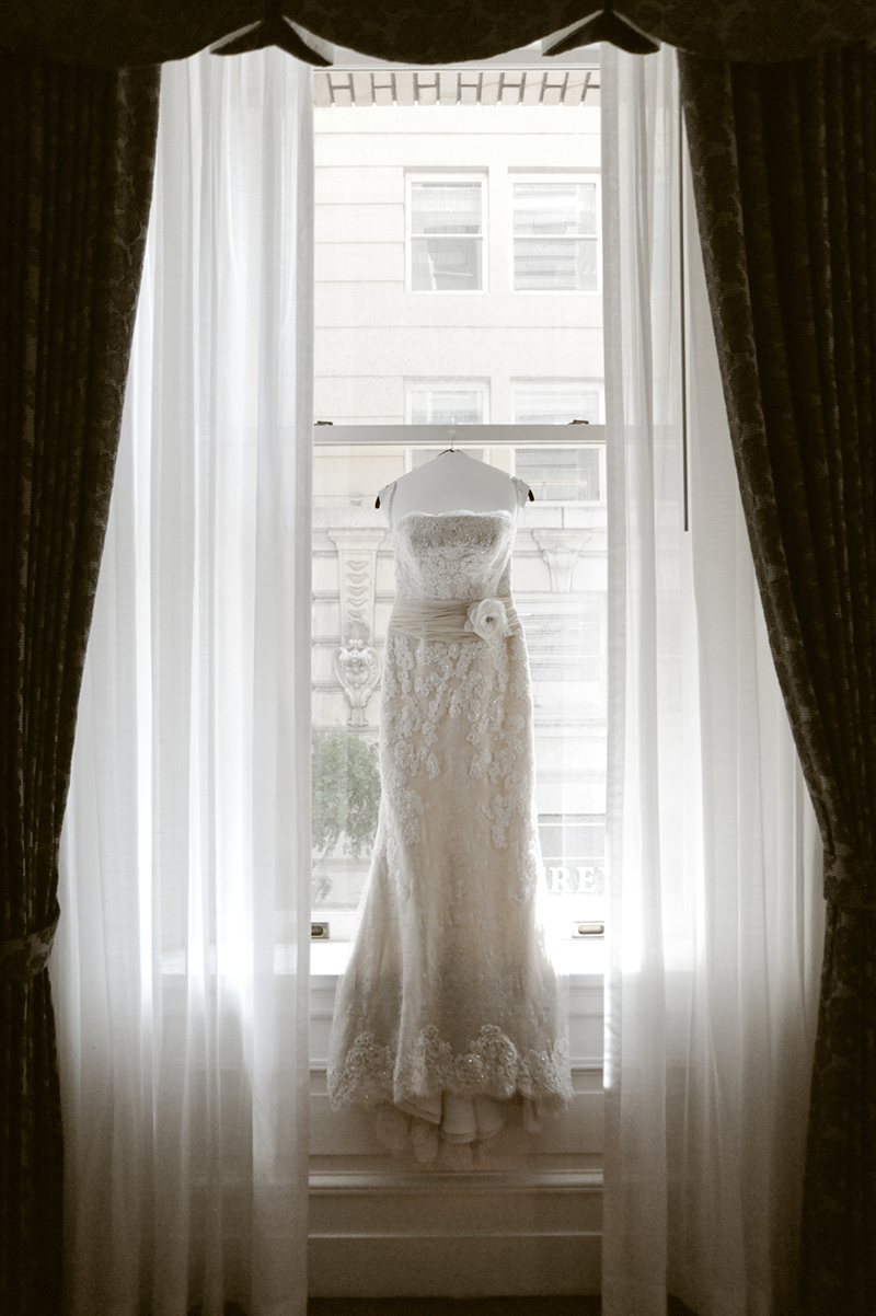 wedding dress hanging in window framed by white and dark grey curtains