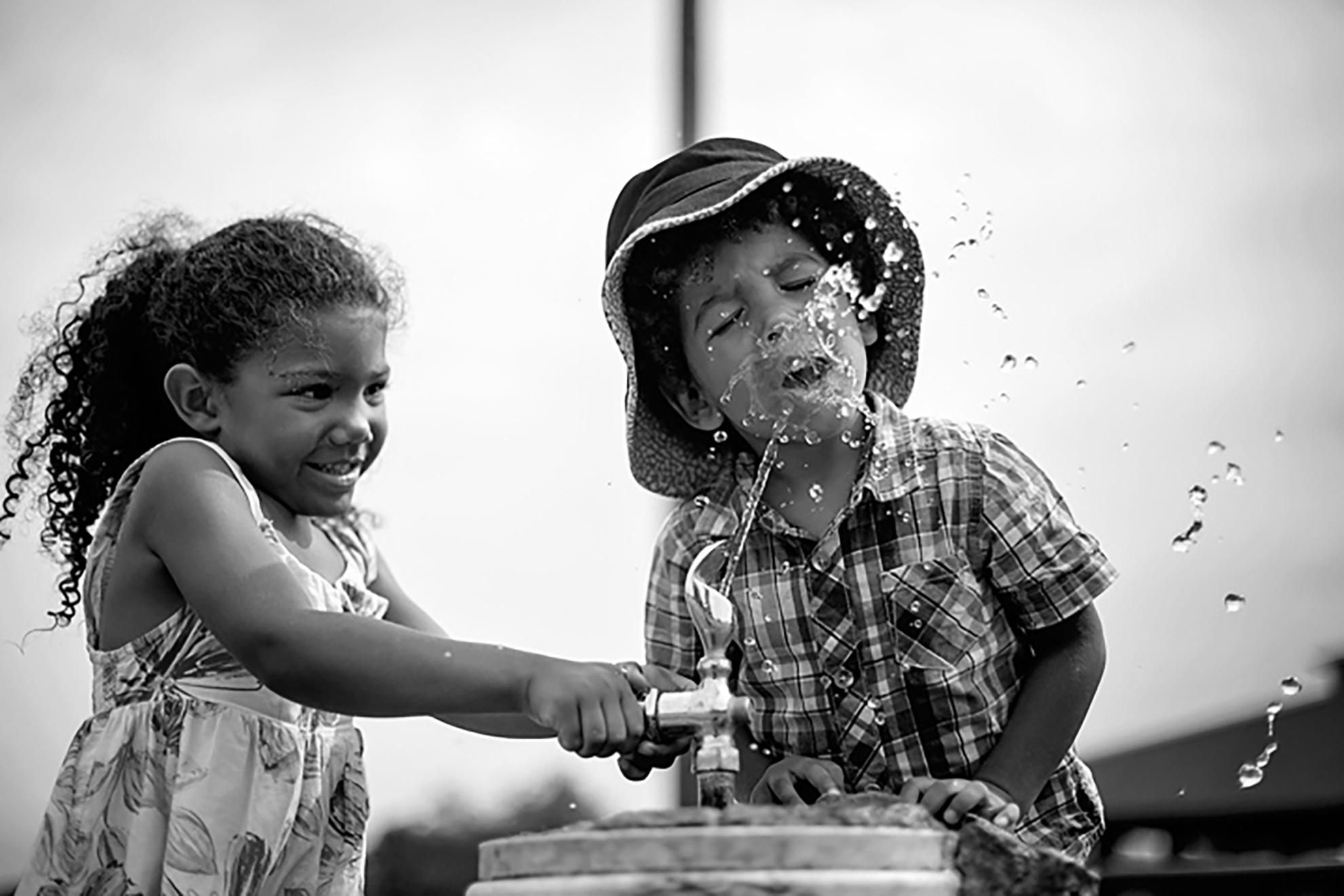 little girl spraying water fountain water into a little boy's face