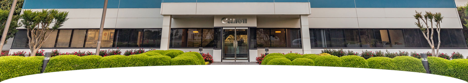 Image of the front face of the Canon Virginia Office building front door with bushes nearby