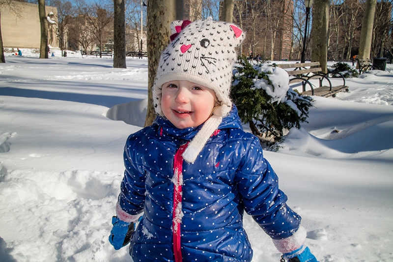 Young girl in blue polka dot parka and cat snow hat smiling at the camera