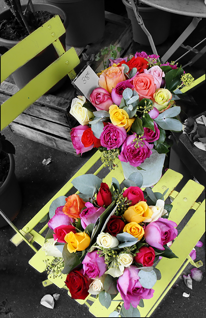 Two brightly colored bouquets of various flowers sitting on a yellow-green metal slotted chair with a muted black and white background