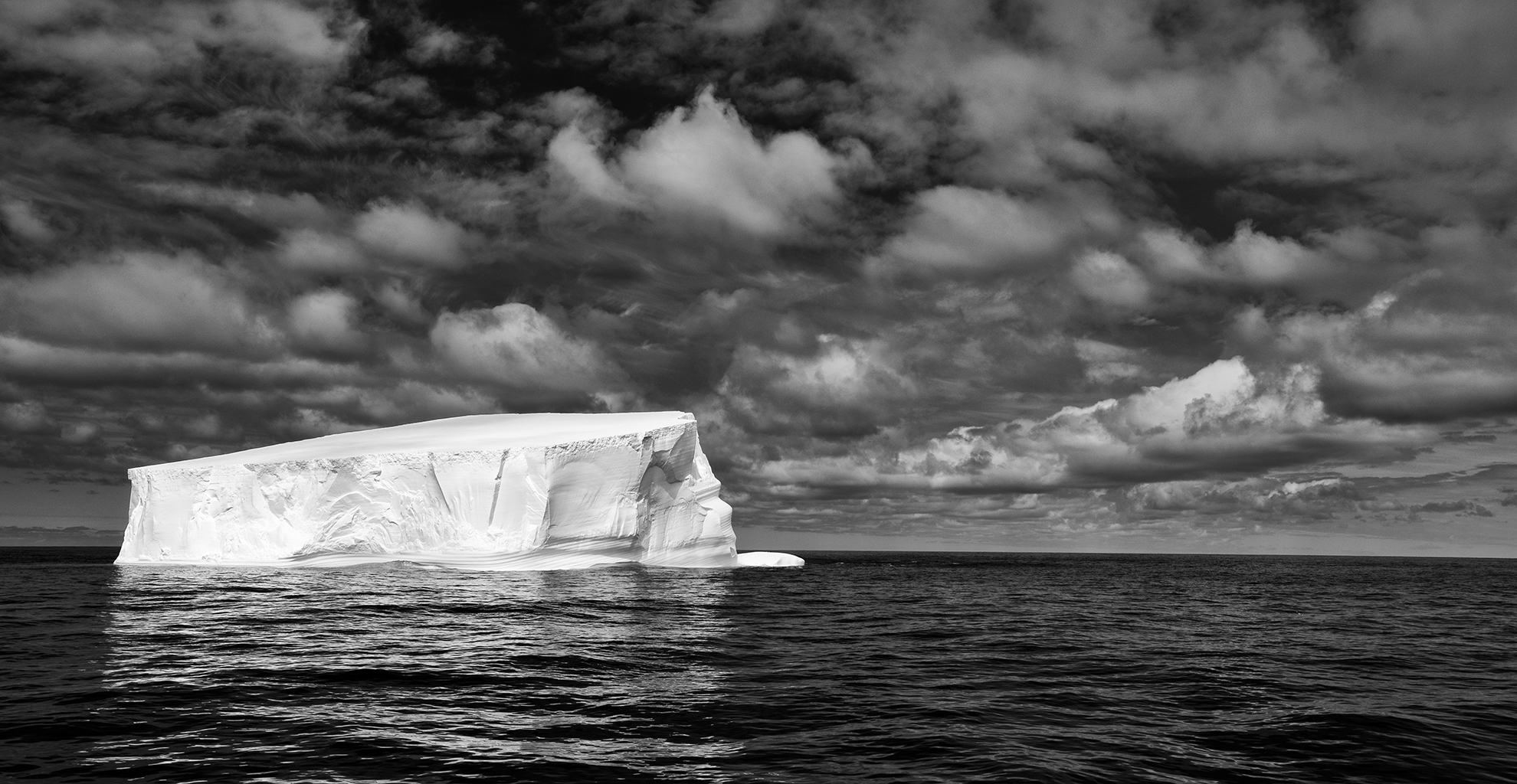black and white image of a lone iceberg in the middle of a sea of water