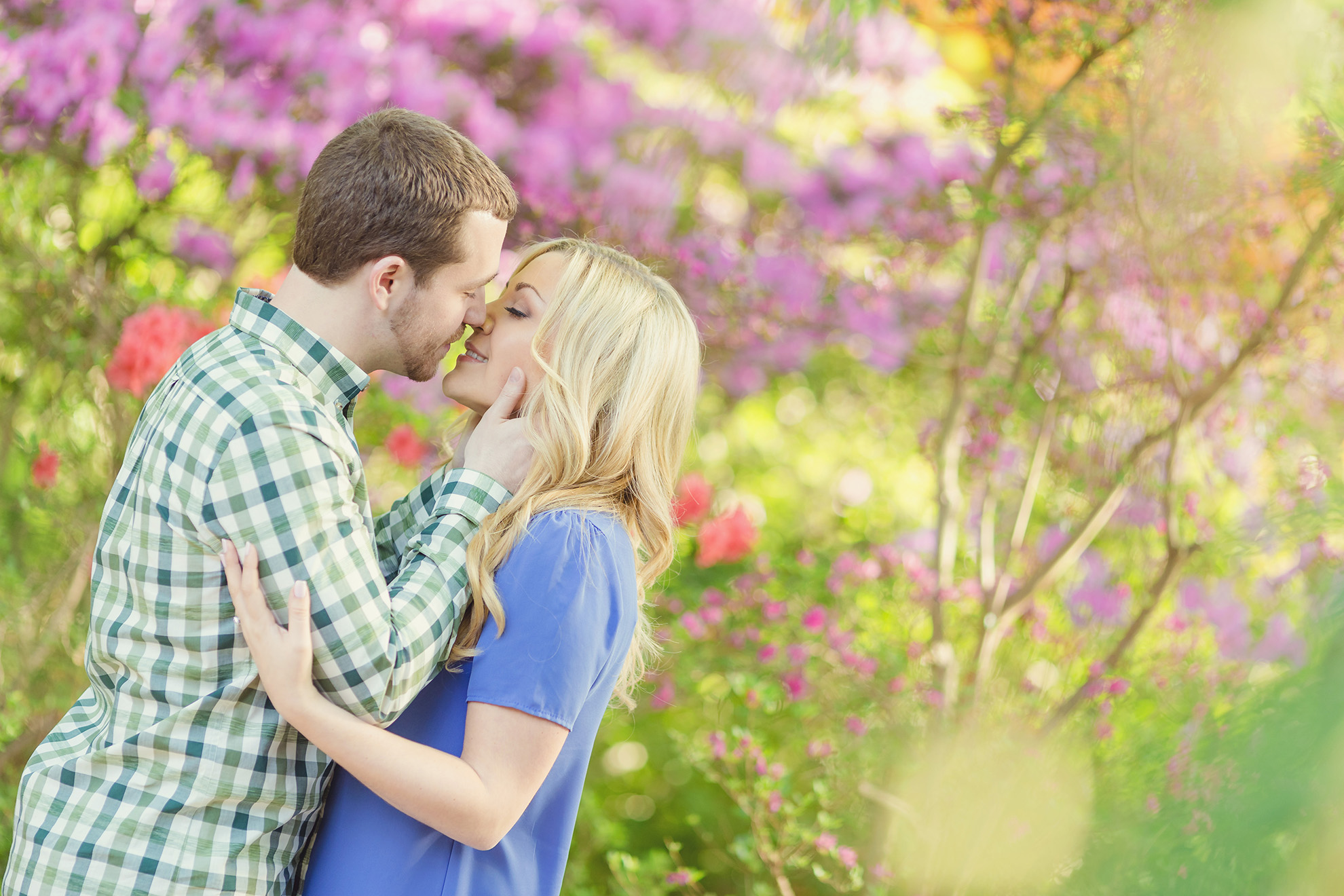 Image of an engaged couple embracing in front fo purple and pink flowered bushes