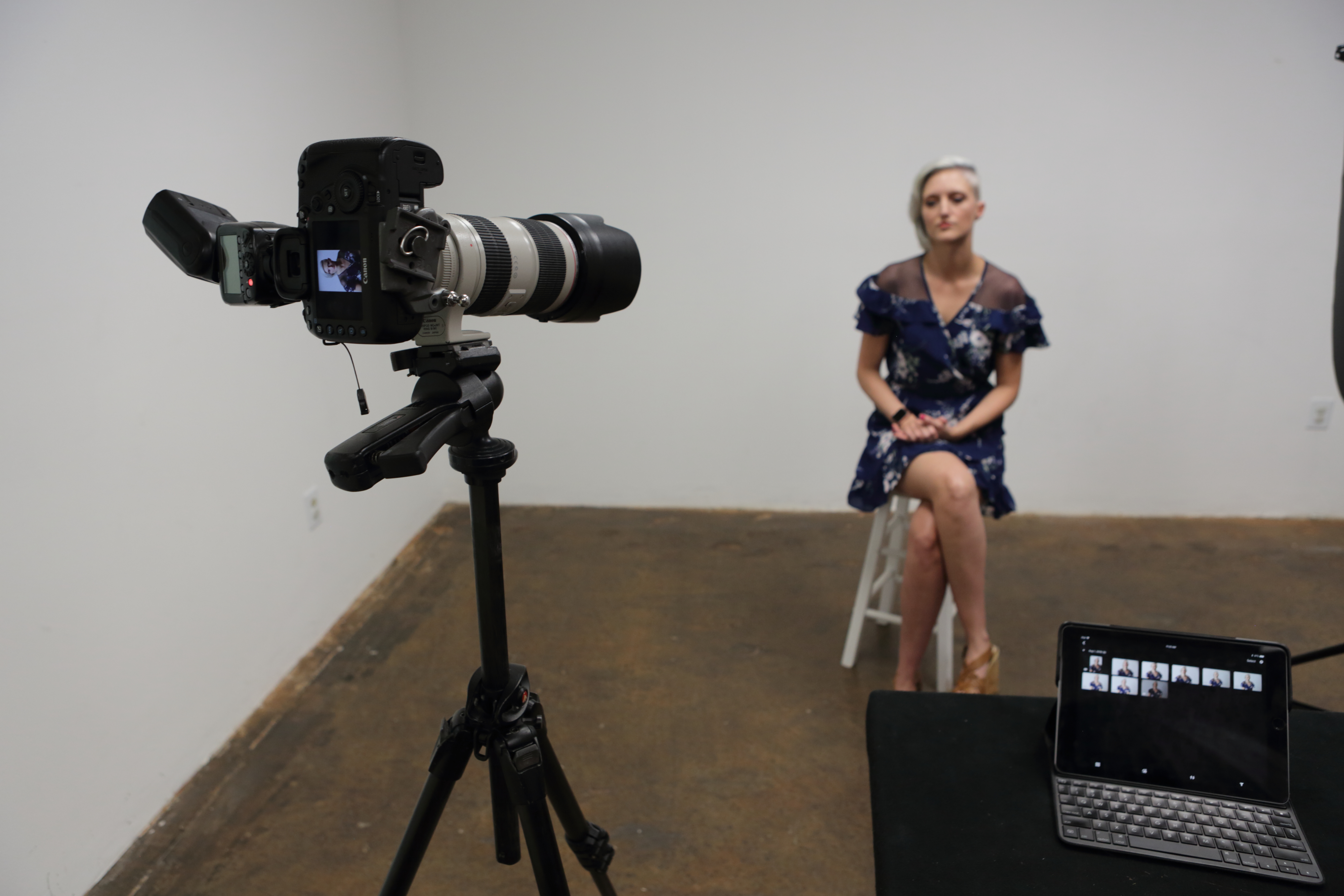 Action shot of camera and speedlite photographing blonde model in blue dress showcasing the distance between the camera and flash to the wall as well as the tablet used