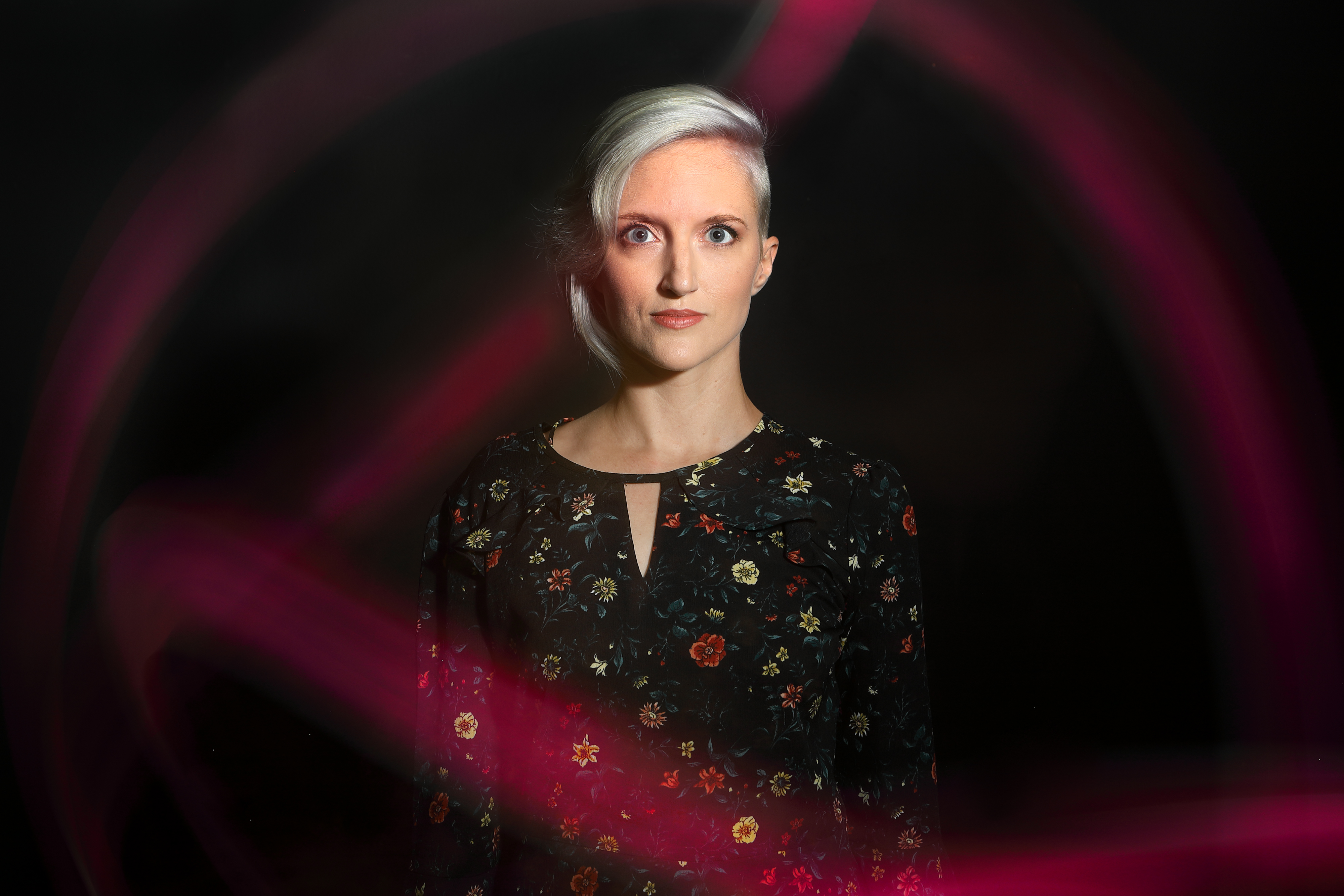 Portrait of blonde model with a dark floral dress surrounded by magenta sweeping lights
