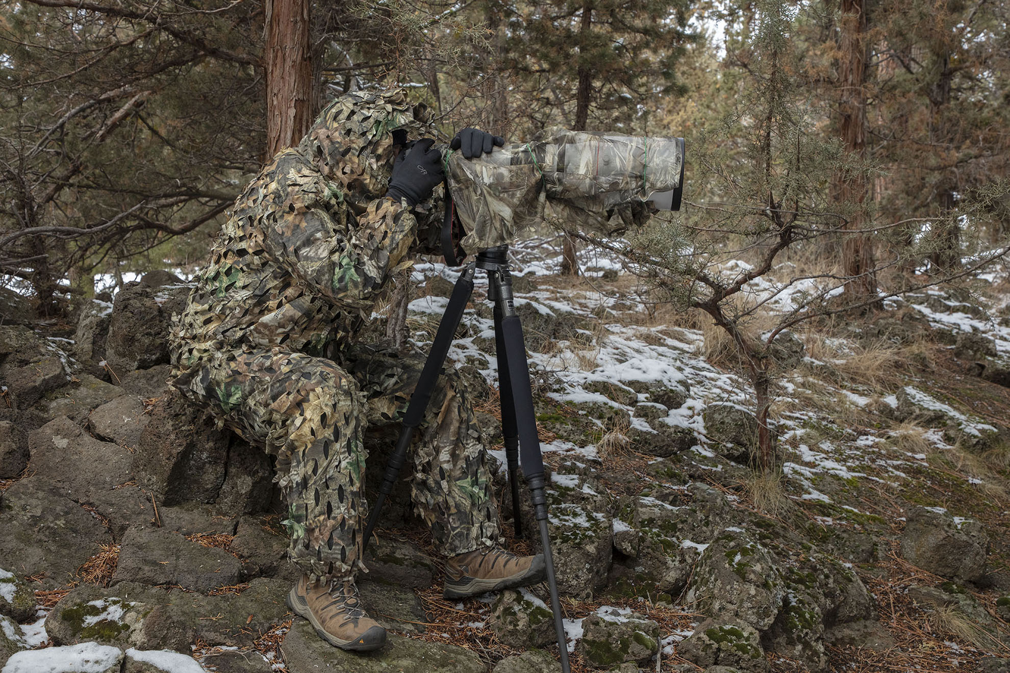 Image of photographer looking through a camera on a tripod with a ghillie camouflage suit