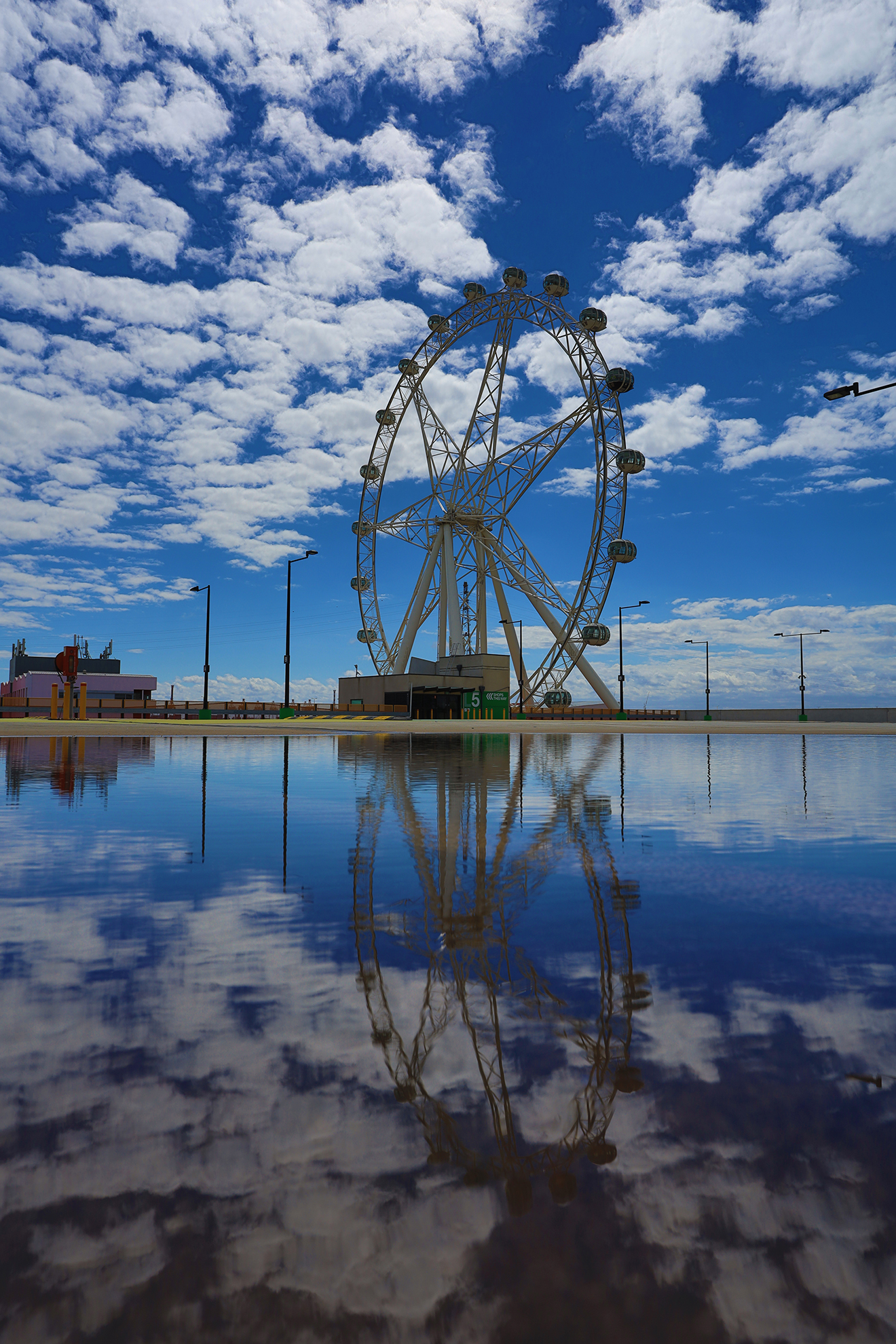 Image of a large ferris wheel image surrounded by a blue sky with white fluffy clouds