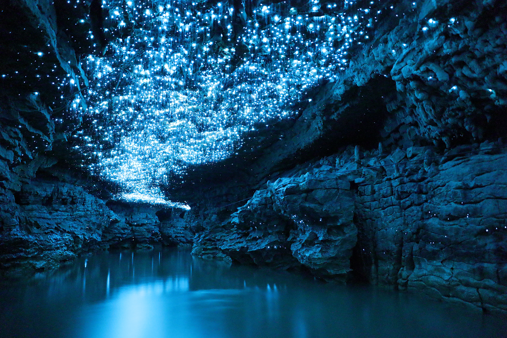 Still water surrounded by a rock formation with a blue hue due to the shimmering blue and white lights at the top of the frame