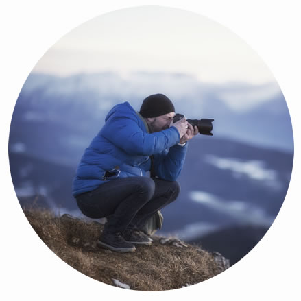 Man crouching and taking a photo over a cliff